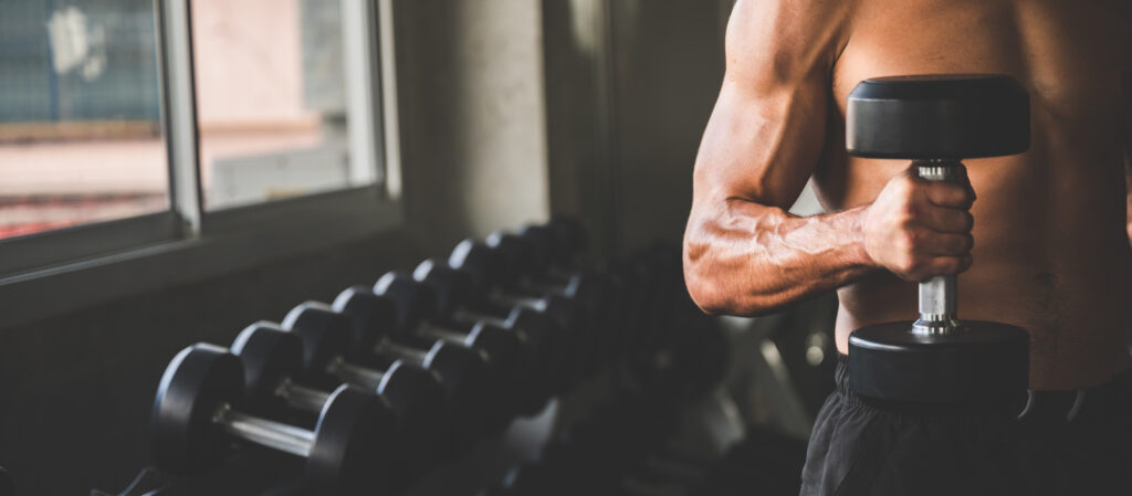 Muscular and strong athletic man exercising with dumbbells in the sport gym, working out concept